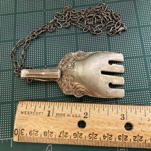 May include: Silver fork necklace with a chain. The fork is about 2 inches long and has a decorative design. The chain is silver and about 18 inches long.