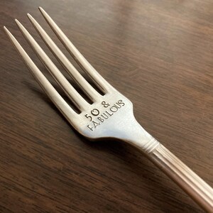 May include: Silver fork with the words "50 & FABULOUS" engraved on the handle.