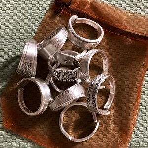 May include: A collection of silver spoon rings in a brown organza bag. The rings are crafted from recycled silverware and feature a range of designs.