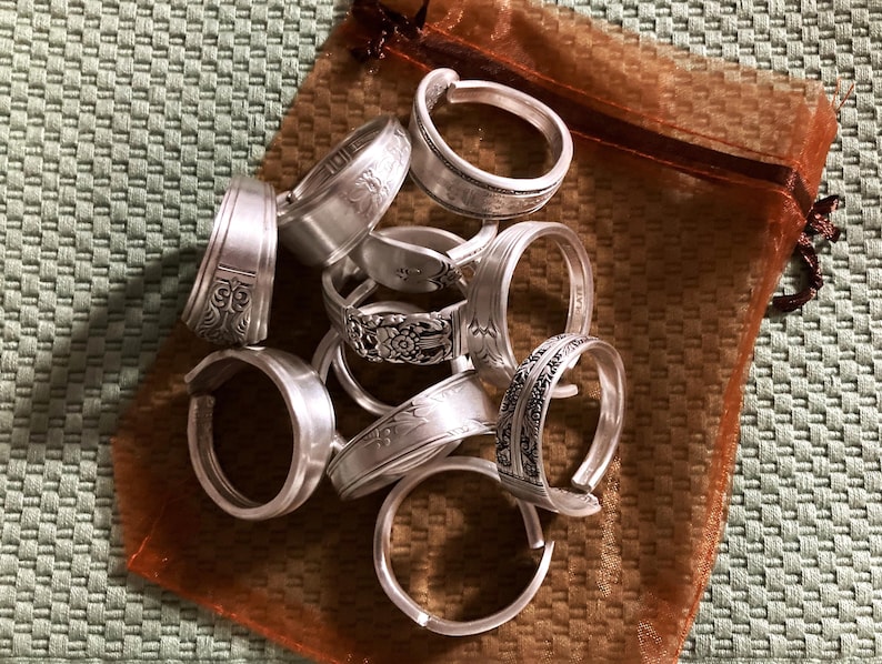 May include: A collection of silver spoon rings in a brown organza bag. The rings are crafted from recycled silverware and feature a range of designs.