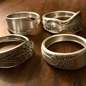 May include: Four silver spoon rings with different designs. Two rings have floral patterns, one has a plain design, and one has a leaf pattern.