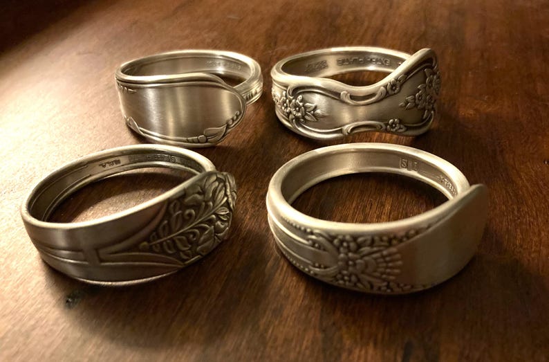 May include: Four silver spoon rings with different designs. Two rings have floral patterns, one has a plain design, and one has a leaf pattern.