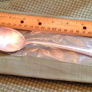 May include: A silver spoon with a personalized inscription that reads "mackenzie's spour". The spoon is packaged in a clear plastic bag.