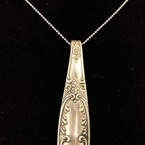 May include: A silver necklace with a pendant made from a vintage spoon. The spoon has an ornate design with floral motifs.