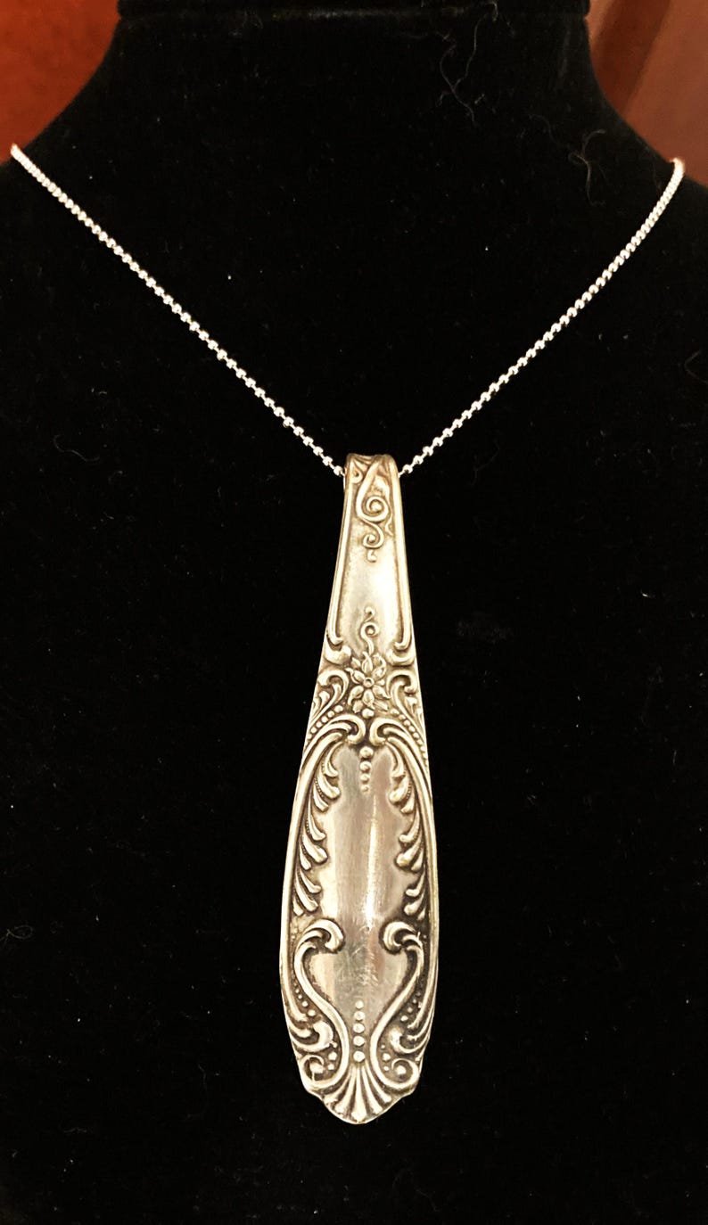 May include: A silver necklace with a pendant made from a vintage spoon. The spoon has an ornate design with floral motifs.