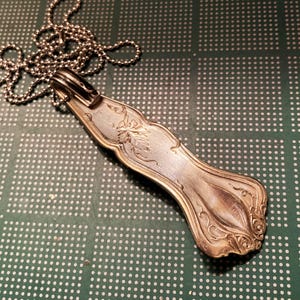 May include: A silver spoon pendant necklace with an ornate design. The spoon is attached to a silver chain.