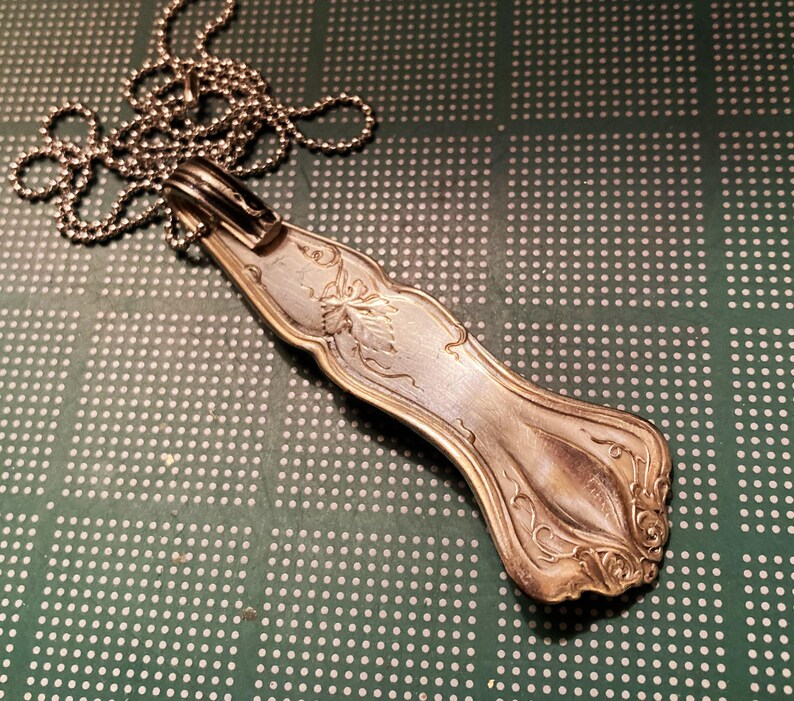 May include: A silver spoon pendant necklace with an ornate design. The spoon is attached to a silver chain.
