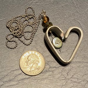 May include: A silver heart-shaped pendant necklace with a silver chain. The pendant has a small green and brown bead and a silver charm inside.