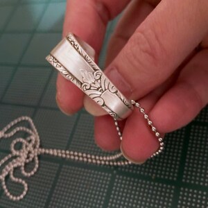 Puede incluir: Un collar de plata con una cuchara adornada con un dise&ntilde;o floral detallado. El collar est&aacute; hecho con una cadena de bolas de plata.