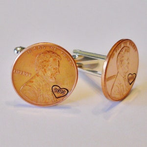 May include: A pair of copper cufflinks featuring a penny with a heart and the year 2012 engraved on it.