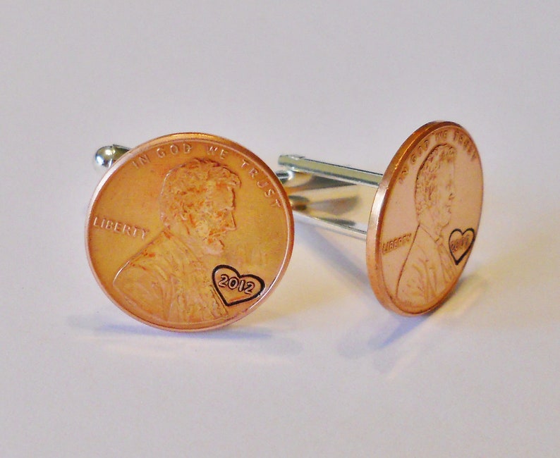 May include: A pair of copper cufflinks featuring a penny with a heart and the year 2012 engraved on it.