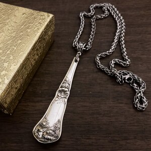 May include: A silver spoon necklace with a floral design. The spoon is attached to a silver chain.