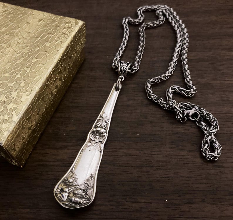 May include: A silver spoon necklace with a floral design. The spoon is attached to a silver chain.
