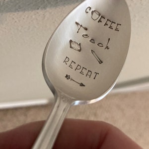May include: A silver spoon with the words "Coffee Teach Repeat" engraved on it. The spoon also has a small coffee cup, book, and pencil engraved on it.