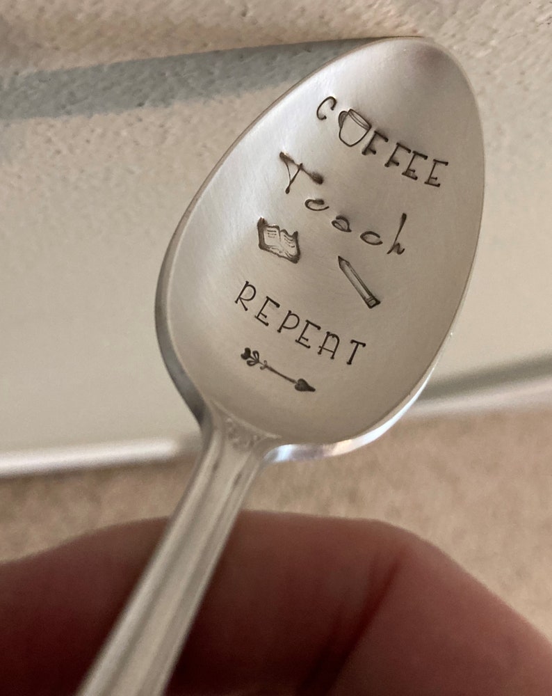 May include: A silver spoon with the words "Coffee Teach Repeat" engraved on it. The spoon also has a small coffee cup, book, and pencil engraved on it.