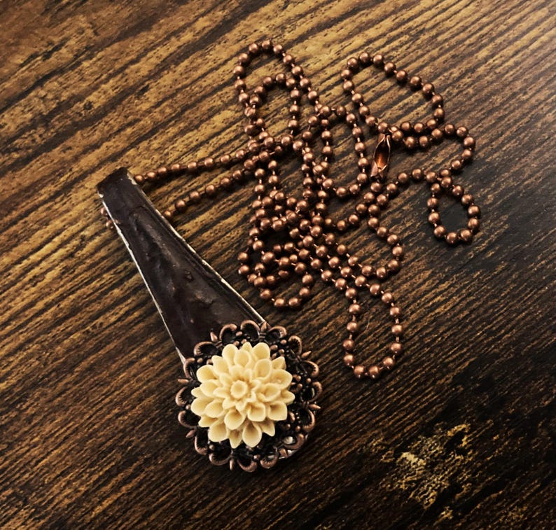 May include: A copper chain necklace with a pendant featuring a brown, textured, rectangular piece with a cream-coloured flower.