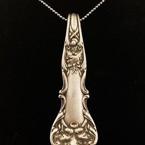 May include: A silver necklace with a pendant made from an ornate antique spoon. The spoon has an intricate design of leaves and swirls.