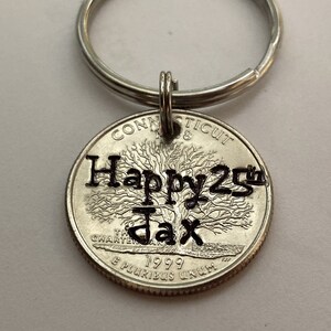 May include: A silver keychain with a Connecticut quarter coin pendant. The coin is engraved with "Happy 25th Jax" and the year 1999. The keychain has a silver ring.