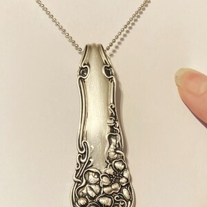 May include: A silver necklace with a pendant made from a vintage spoon. The spoon has a floral design and is polished to a shine.