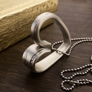 May include: A silver heart-shaped pendant necklace made from a repurposed spoon. The pendant has a detailed floral design and is attached to a silver ball chain.