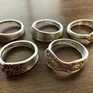 Puede incluir: Cinco anillos de servilleta de plata hechos con cubiertos reutilizados con dise&ntilde;os florales ornamentados.