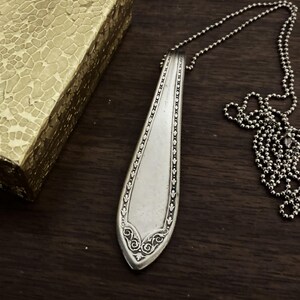 May include: A silver spoon pendant necklace with an ornate design. The spoon is attached to a silver chain.