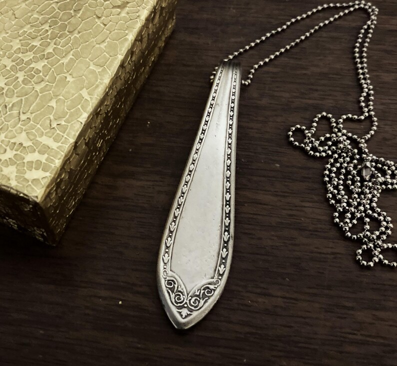 May include: A silver spoon pendant necklace with an ornate design. The spoon is attached to a silver chain.