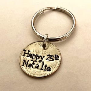 May include: A silver keychain with a round charm. The charm is a Maryland quarter with the words "Happy 25th Natalie" stamped on it. The year 2000 is also visible on the quarter.