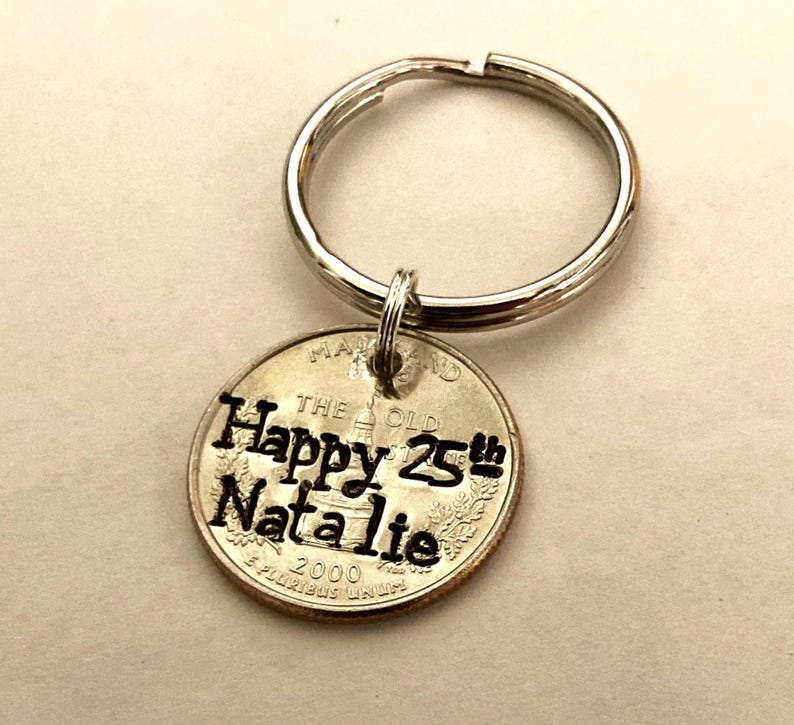 May include: A silver keychain with a round charm. The charm is a Maryland quarter with the words "Happy 25th Natalie" stamped on it. The year 2000 is also visible on the quarter.