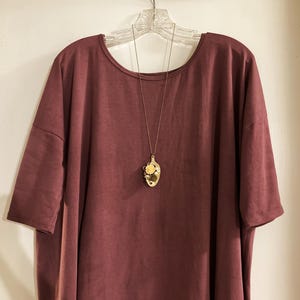 May include: A maroon colored, loose-fitting, short-sleeved t-shirt with a gold spoon pendant necklace. The spoon has a floral design.