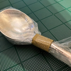 May include: A silver chili spoon with the words "Come get a Chili Spoon" engraved on the bowl. The spoon is wrapped in clear plastic and a brown tape.