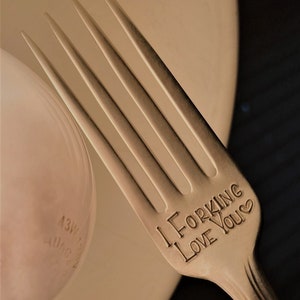 Op de afbeelding: Een zilveren vork met de woorden "I Forking Love You" gegraveerd op het handvat. De vork ligt op een wit bord.