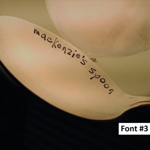 May include: A close-up of a beige spoon with the words "mackenzie's spoon" written on it in black ink.