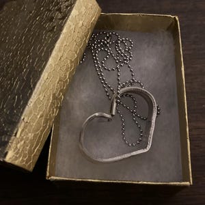 May include: A silver heart-shaped pendant necklace with a silver chain in a gold box.