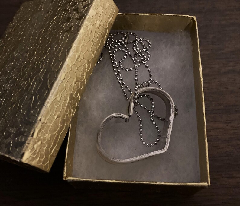 May include: A silver heart-shaped pendant necklace with a silver chain in a gold box.