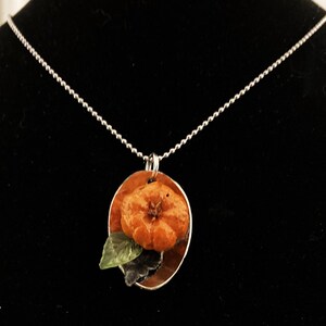 May include: A silver chain necklace with a round pendant featuring a small orange flower with green leaves. The pendant is set on a silver background.