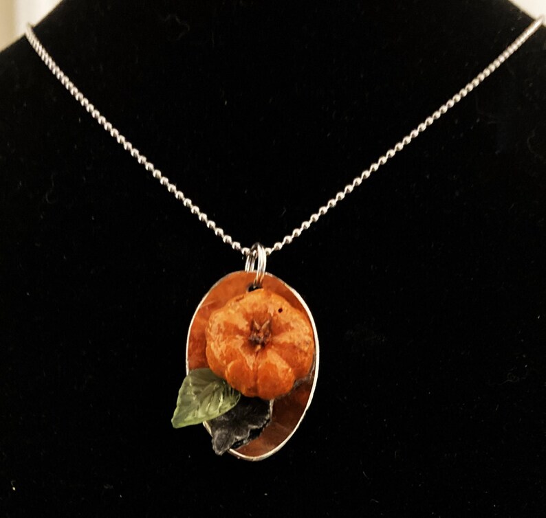 May include: A silver chain necklace with a round pendant featuring a small orange flower with green leaves. The pendant is set on a silver background.