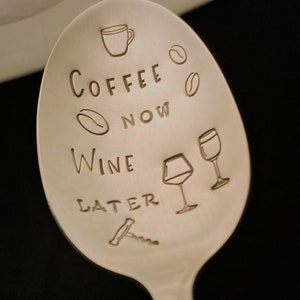 May include: A silver spoon with the text "Coffee Now Wine Later" engraved on it. The spoon also features a coffee cup, coffee beans, wine glasses, and a corkscrew.