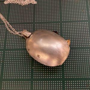 May include: A silver spoon pendant necklace with a chain. The spoon is closed and has a shiny finish.