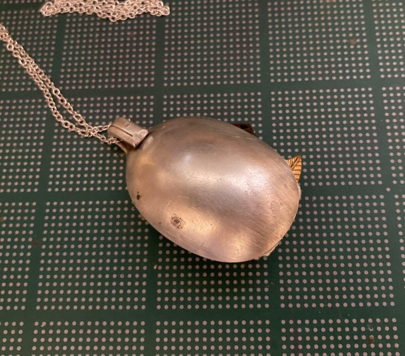 May include: A silver spoon pendant necklace with a chain. The spoon is closed and has a shiny finish.