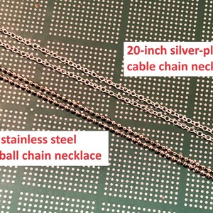 May include: Two silver chains on a green background. The top chain is a 20-inch silver-plated cable chain necklace. The bottom chain is a 20-inch stainless steel 1.5mm ball chain necklace.