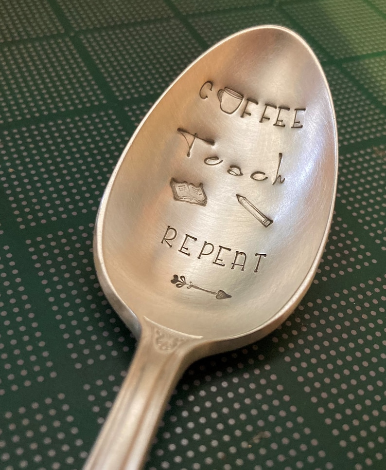 May include: A silver spoon with the words "Coffee Teach Repeat" engraved on it. The spoon also has small illustrations of a coffee cup, a book, a pencil, and an arrow.