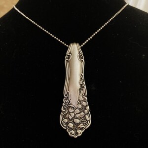 May include: A silver spoon necklace with a floral design. The spoon is attached to a silver chain.