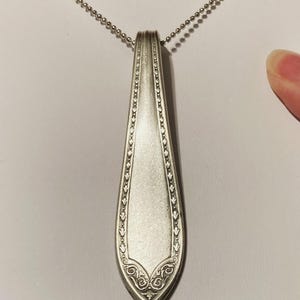 May include: A silver spoon pendant necklace with a decorative design on the handle. The spoon is attached to a silver chain.