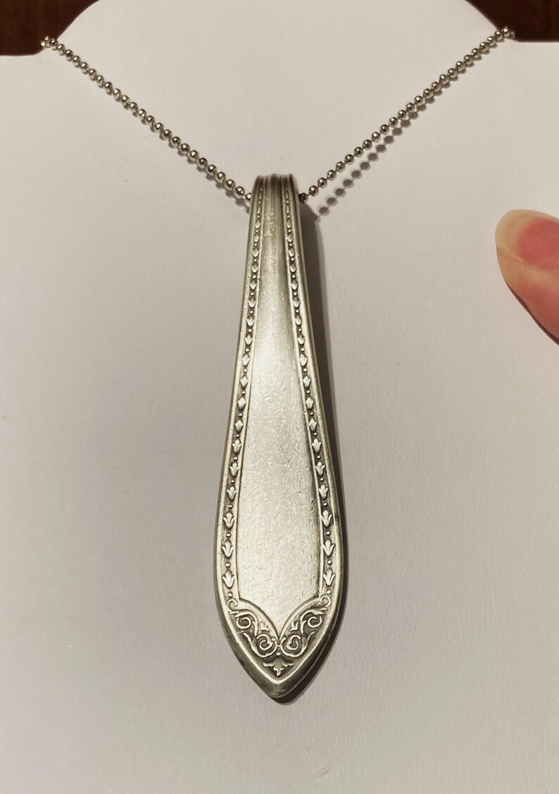 May include: A silver spoon pendant necklace with a decorative design on the handle. The spoon is attached to a silver chain.