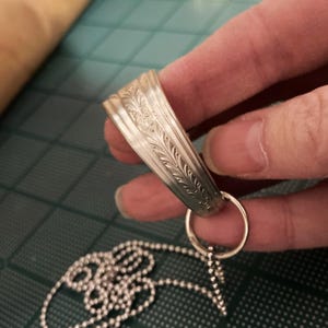 May include: A silver chain necklace with a decorative pendant. The pendant is a silver ring with an ornate design.