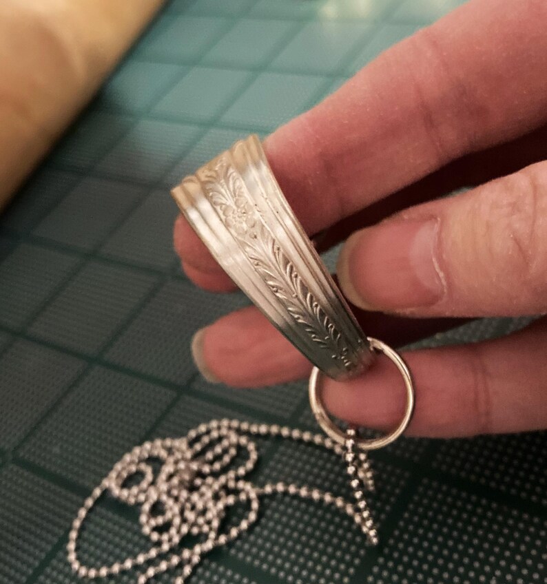 May include: A silver chain necklace with a decorative pendant. The pendant is a silver ring with an ornate design.
