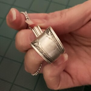 May include: A silver spoon ring with a decorative design. The ring is made from a repurposed spoon.