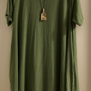 May include: A green short-sleeved dress with a round neckline. A silver chain necklace with a gold pendant hangs from the neckline.