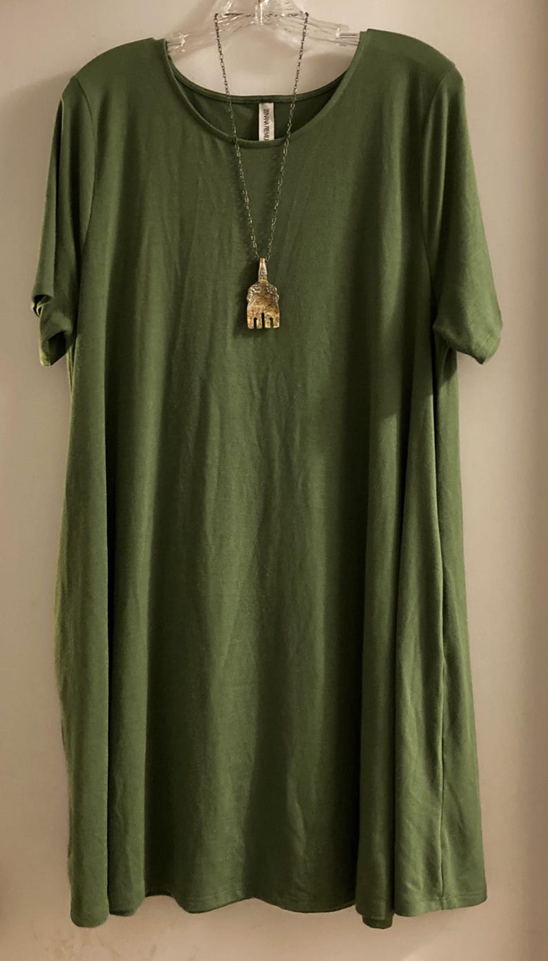 May include: A green short-sleeved dress with a round neckline. A silver chain necklace with a gold pendant hangs from the neckline.